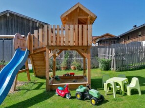 A wooden playhouse with a slide, surrounded by toys and a picnic table. - Holiday Apartment in Leogang with Mountain View (Leogang)