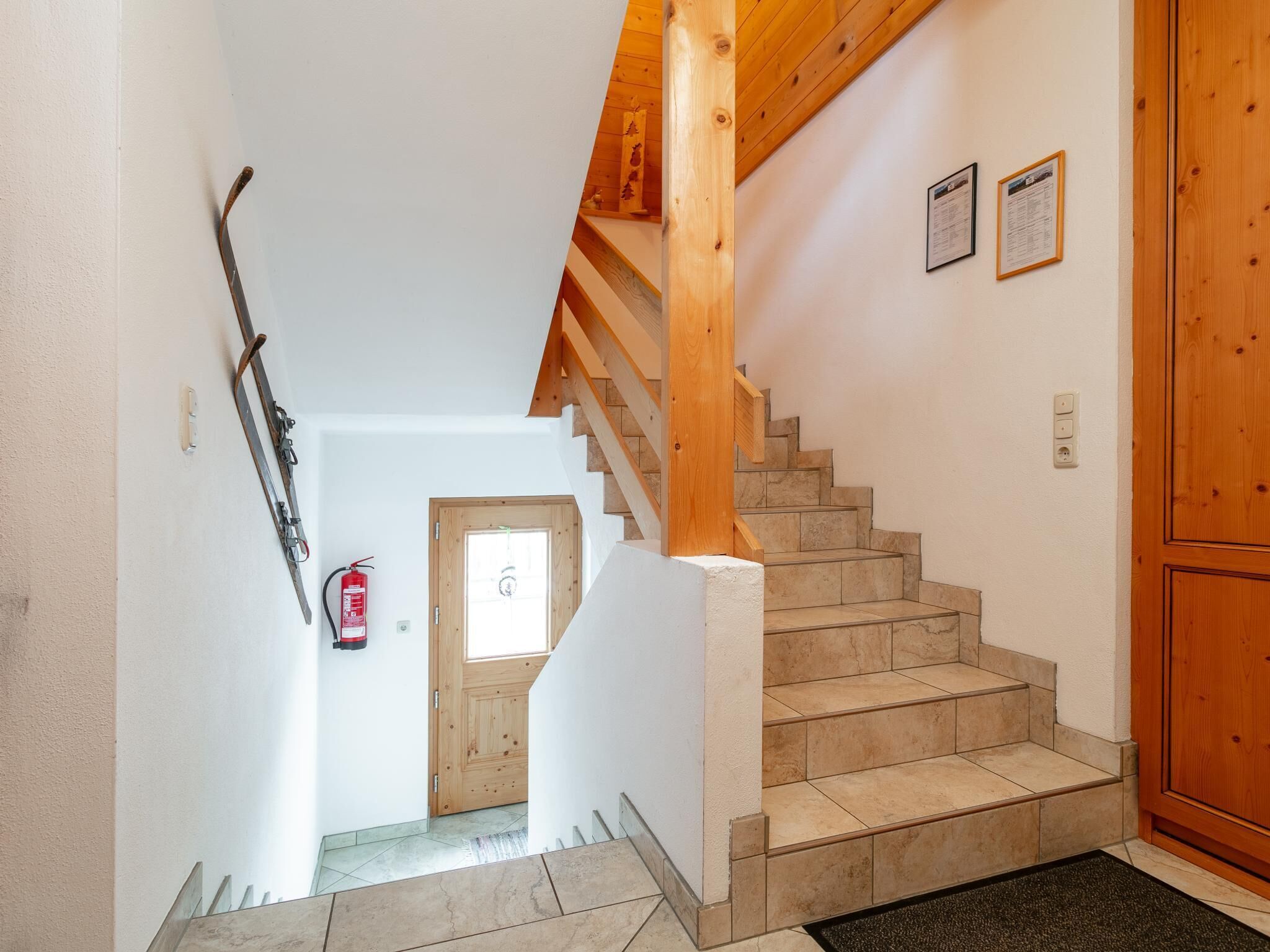 Eine Treppe mit Holelllaufgeländern und beigen Fliesen, die zu einer Tür mit Fenster führt.