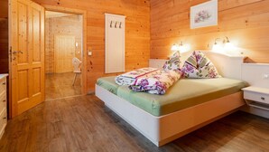 Un dormitorio con paneles de madera, una cama, mesitas de noche y una puerta que da a otra habitación.