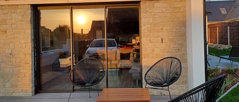 Un edificio moderno con fachada de madera, puerta de entrada de vidrio y un patio con una mesa y dos sillas de madera.