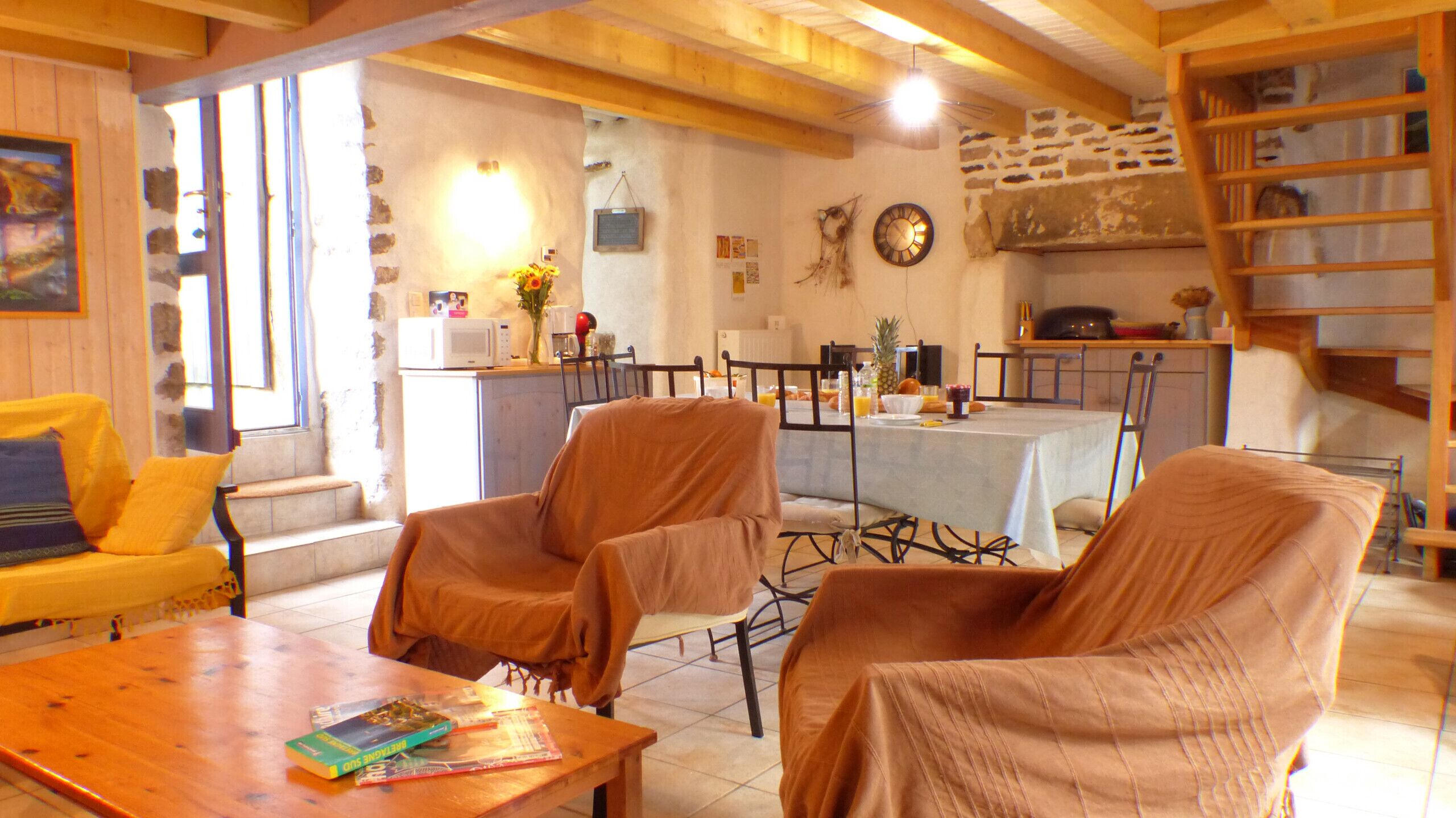 Ein gemütliches Wohnzimmer mit Holztisch, zwei Sesseln, einer Couch und einer Essecke für vier Personen.