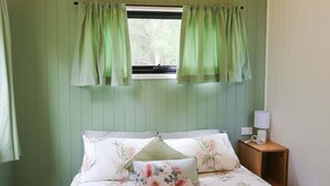 Une chambre à coucher avec un lit, une literie à motifs floraux, une table de chevet avec une lampe et une fenêtre avec des rideaux.