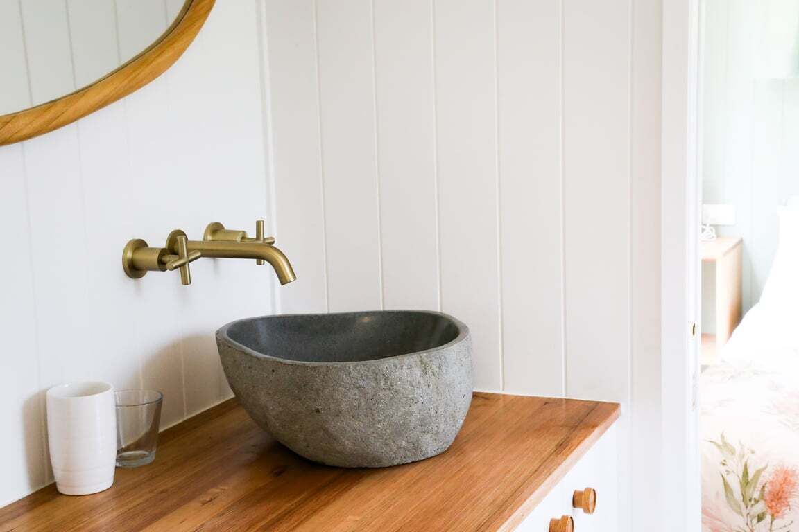 A bathroom with a stone basin sink, brass faucet, and a wooden countertop.