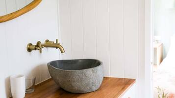 A bathroom with a stone basin sink, brass faucet, and a wooden countertop.