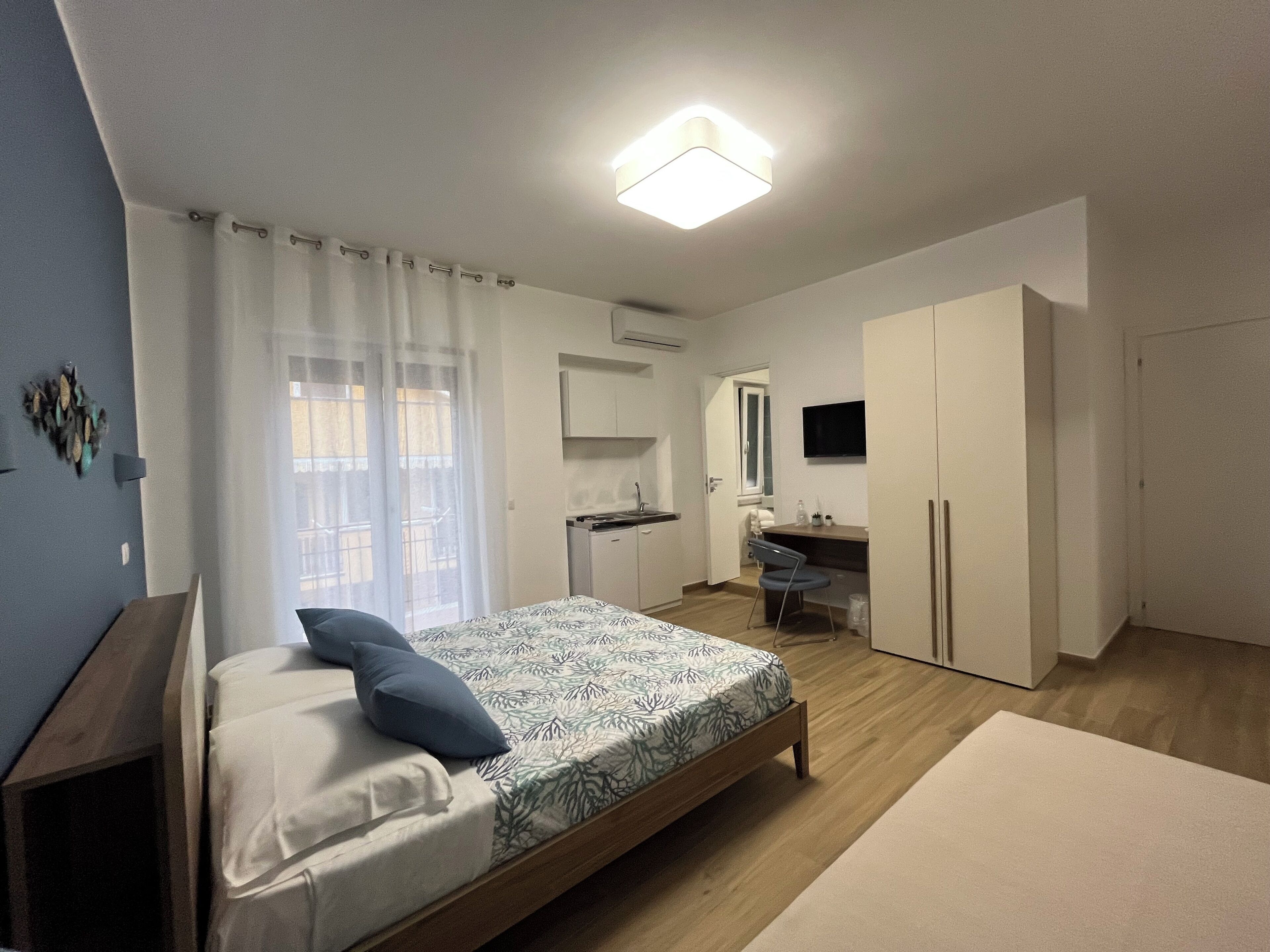 Un dormitorio con cama, escritorio, silla, armario, televisor y ventana con cortinas.