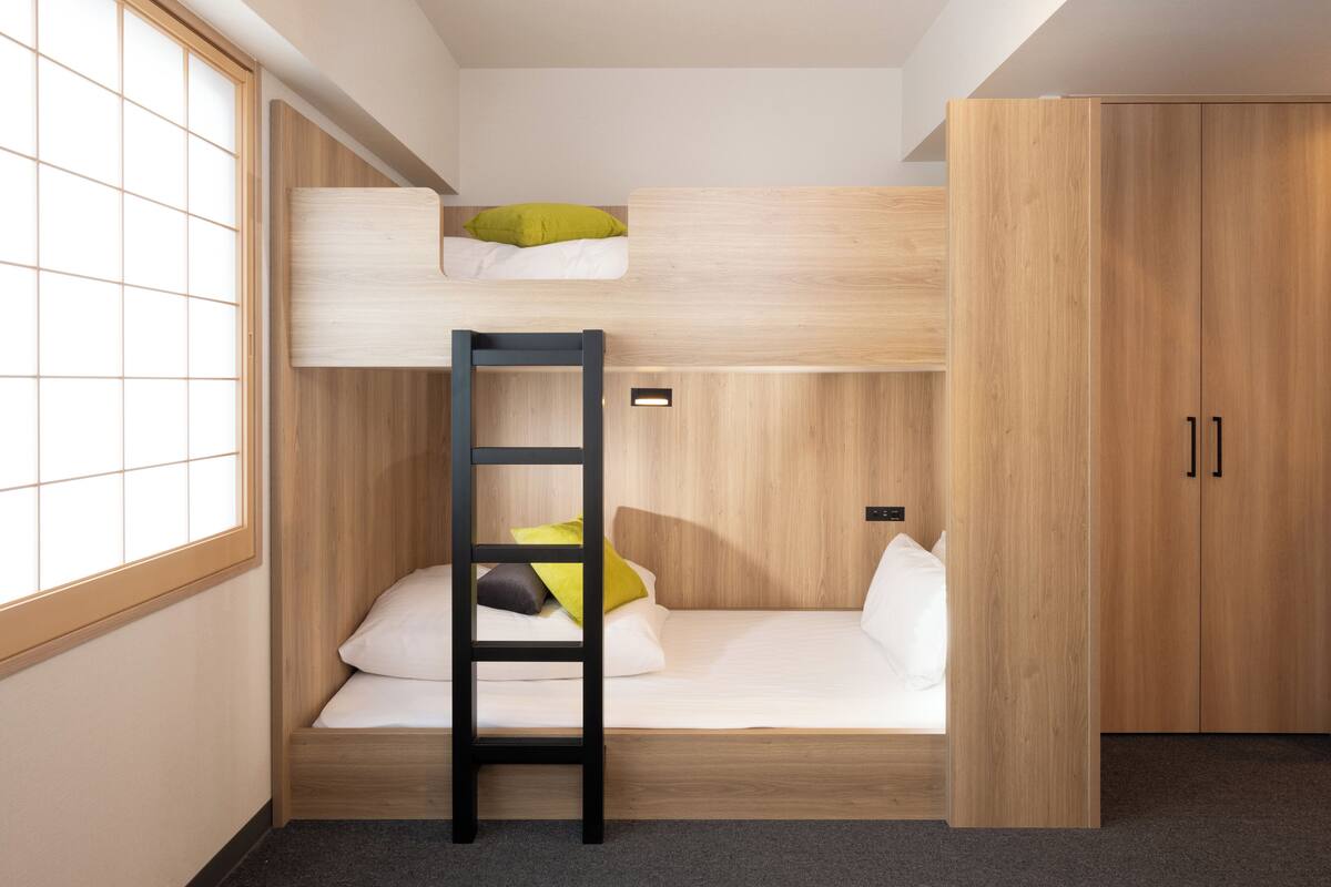 A bunk bed room with a ladder, a wardrobe, and a window.