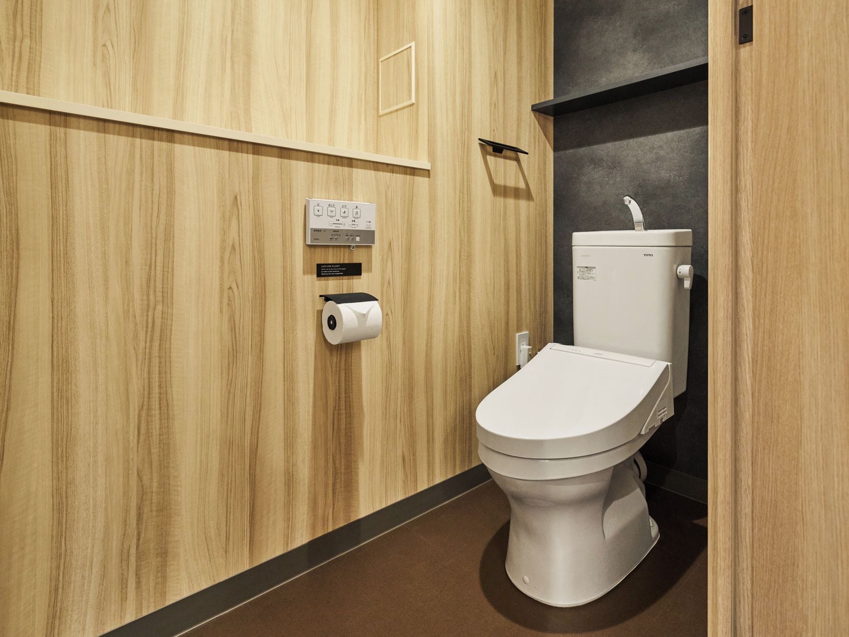 A modern bathroom with a toilet, a paper towel dispenser, and a control panel.