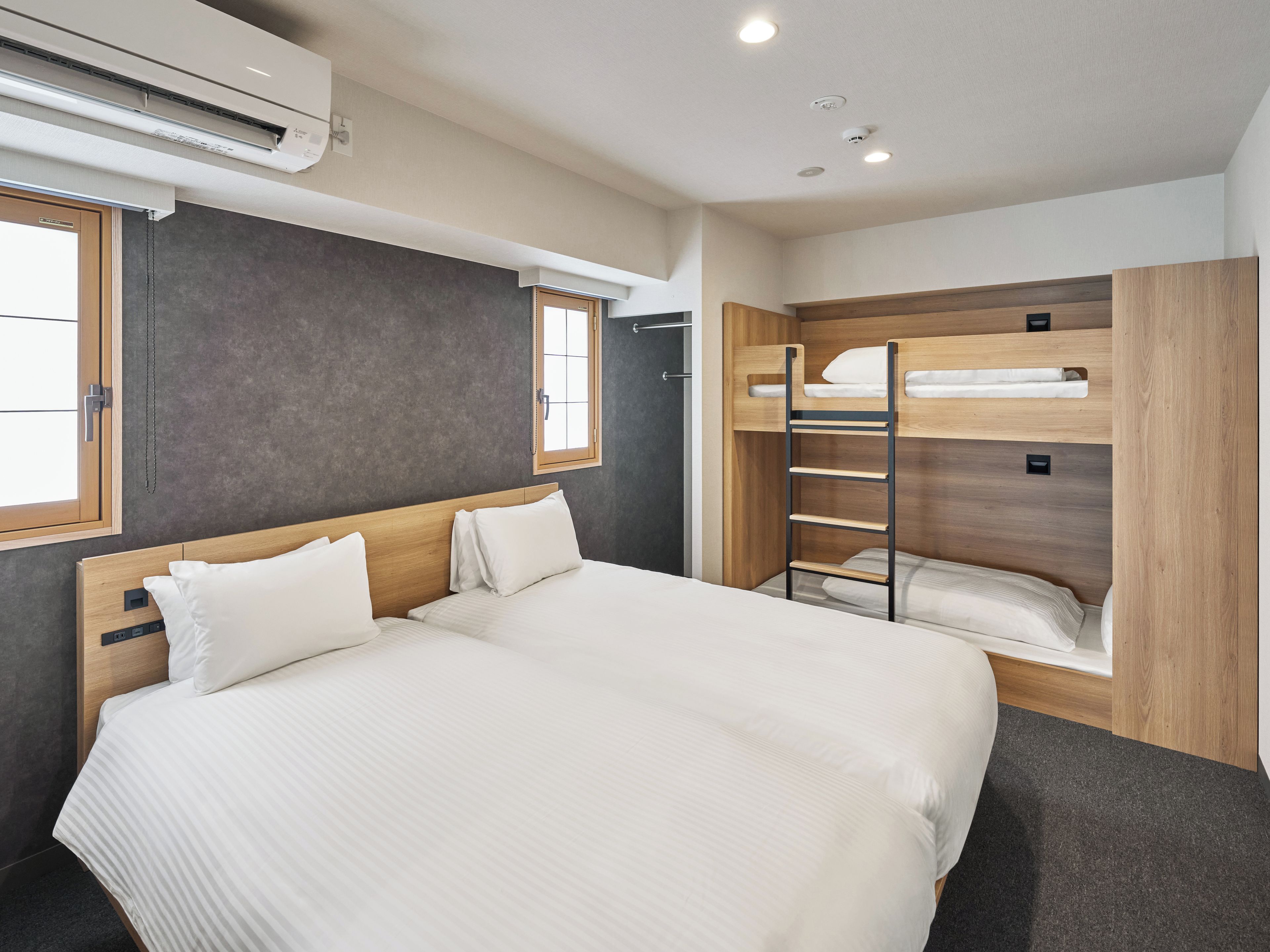 A hotel room with a large bed, a bunk bed, a window, and an air conditioning unit.