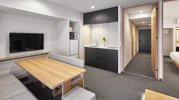 A modern hotel room with a dining area, kitchenette, and a TV mounted on the wall.