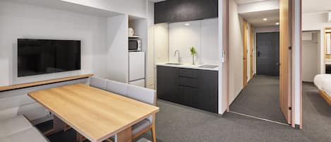 Una habitación de hotel moderna con comedor, kitchenette y un televisor montado en la pared.