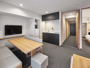 A modern hotel room with a dining area, kitchenette, and a TV mounted on the wall.