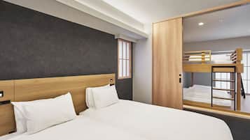 Habitación de hotel moderna con una cama grande, cabecera de madera, armario y una cama litera al fondo.