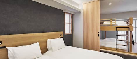 Habitación de hotel moderna con una cama grande, cabecera de madera, armario y una cama litera al fondo.
