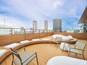 A rooftop terrace with seating areas, a view of the city skyline, and a clear sky.