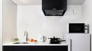 A modern kitchen with a white countertop, a black stove, a white kettle, and a microwave. - MIMARU Osaka Namba Station Annex (Opens on October 1, 2026) (Osaka)