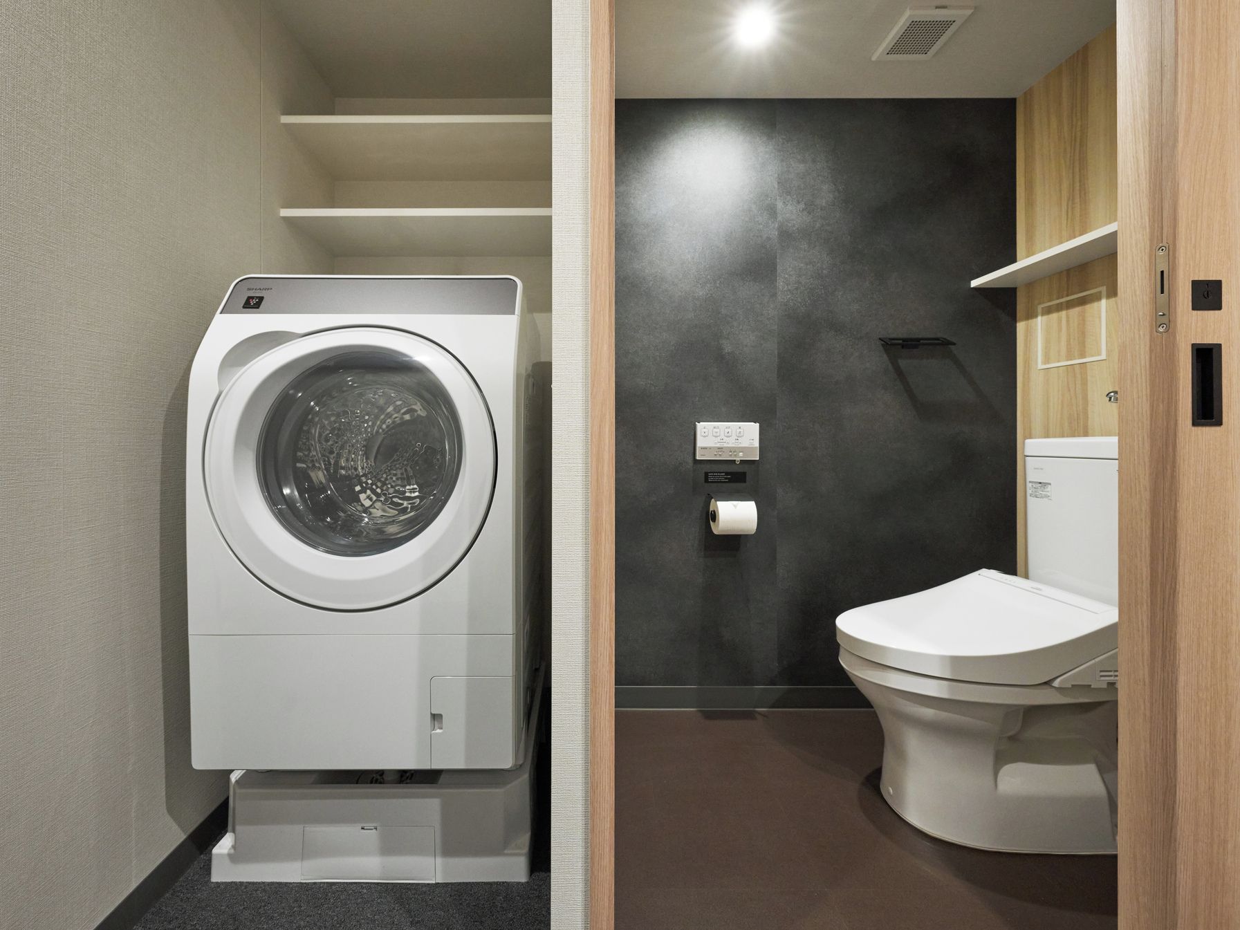 A compact bathroom with a front-loading washing machine, a toilet, and a towel dispenser.