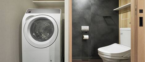 A compact bathroom with a front-loading washing machine, a toilet, and a towel dispenser.