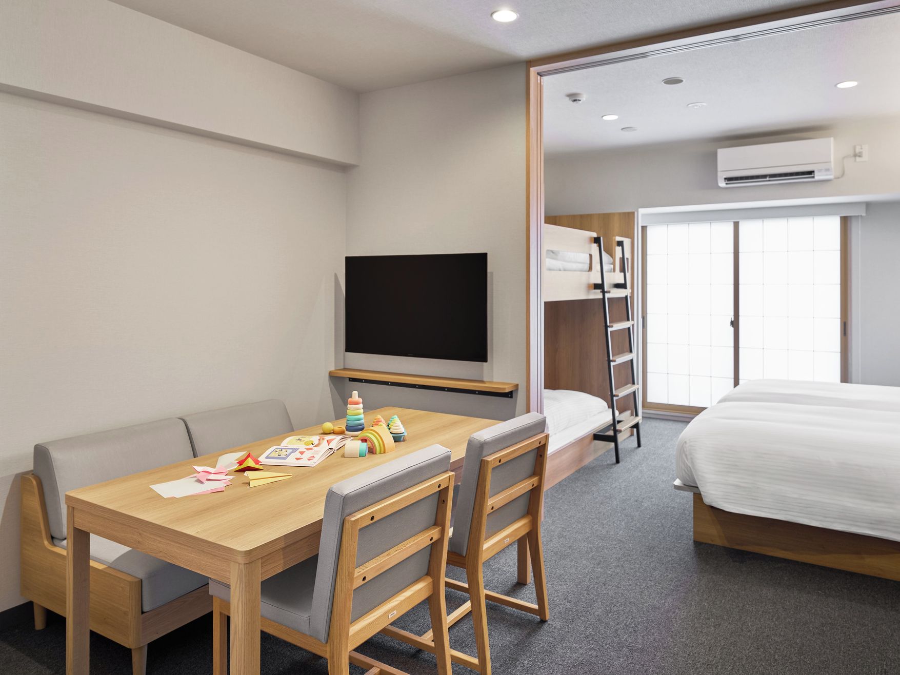 Une chambre d’hôtel avec un bureau en bois, une télévision, un lit superposé et un appareil de climatisation.