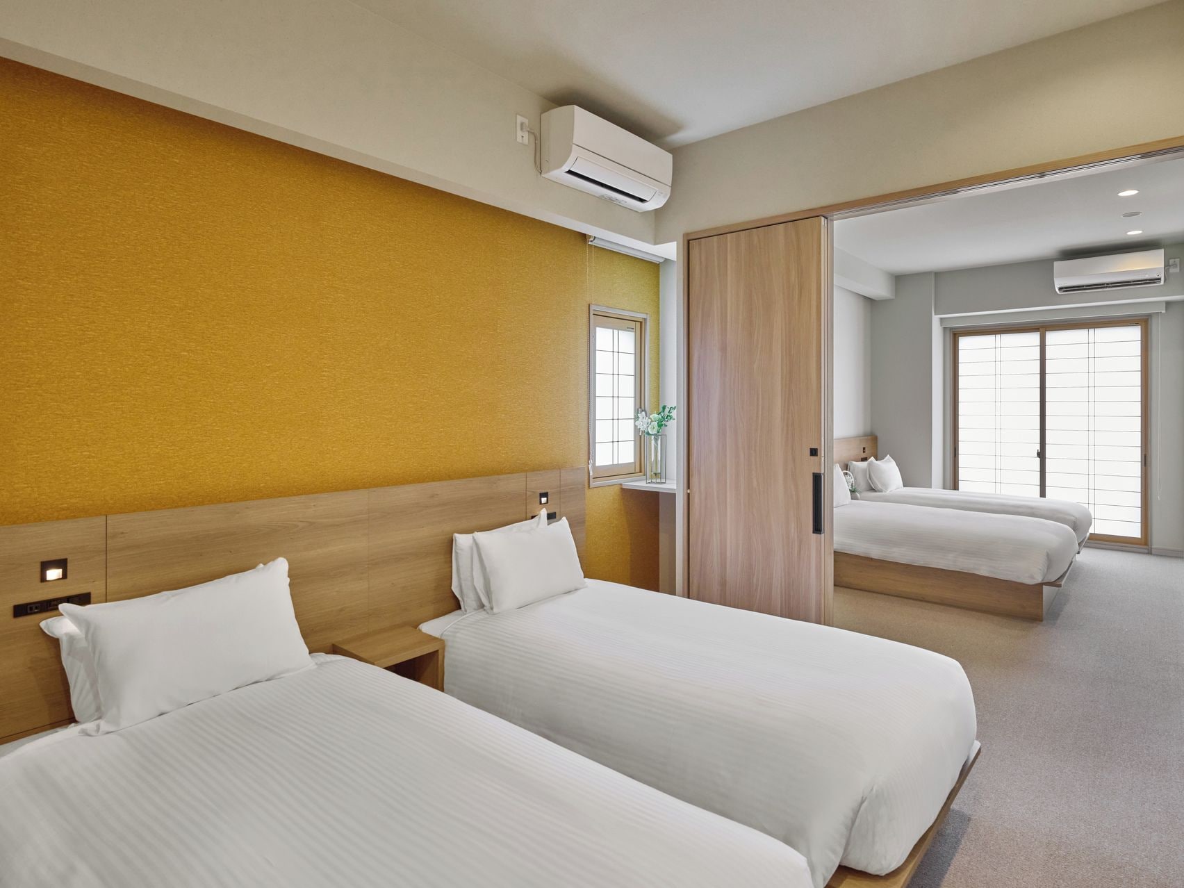 Une chambre d’hôtel avec deux lits, une tête de lit en bois, une fenêtre donnant sur un beau paysage et un appareil de climatisation.