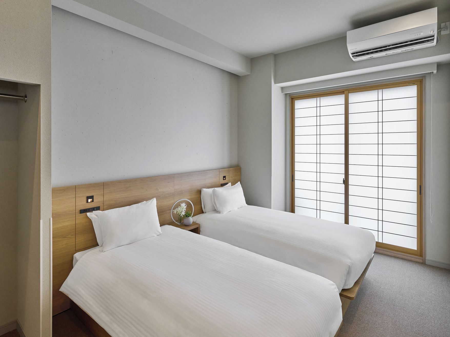 A hotel room with two beds, a wooden headboard, an air conditioning unit, and a sliding door with a grid pattern.