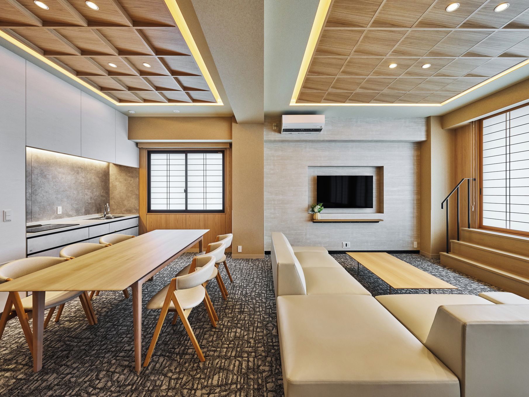 A modern hotel room with a dining area, a sofa set, and a TV mounted on the wall.