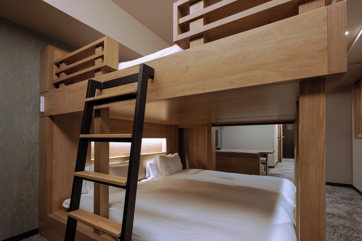 A bunk bed room with a ladder, a desk, and a television in the background.