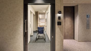 An elevator with a control panel, a wheelchair, and a corridor leading to a room.