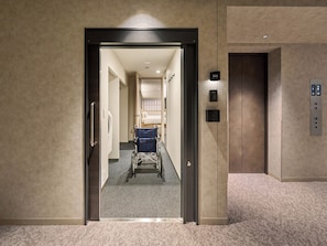 An elevator with a control panel, a wheelchair, and a corridor leading to a room.