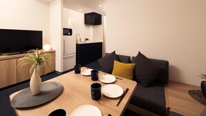 A modern living room with a flat-screen TV, a dining table set with plates and cups, a sofa with cushions, and a kitchen area with a microwave and sink. - MIMARU Osaka Namba Station Annex (Opens on October 1, 2026) (Osaka)