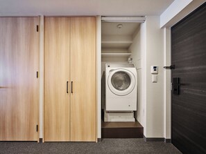 A laundry room with a washing machine, wooden wardrobe, and a dark door.