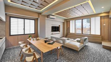 A modern hotel room with a wooden ceiling, a dining area with a table and chairs, a sofa, and large windows.