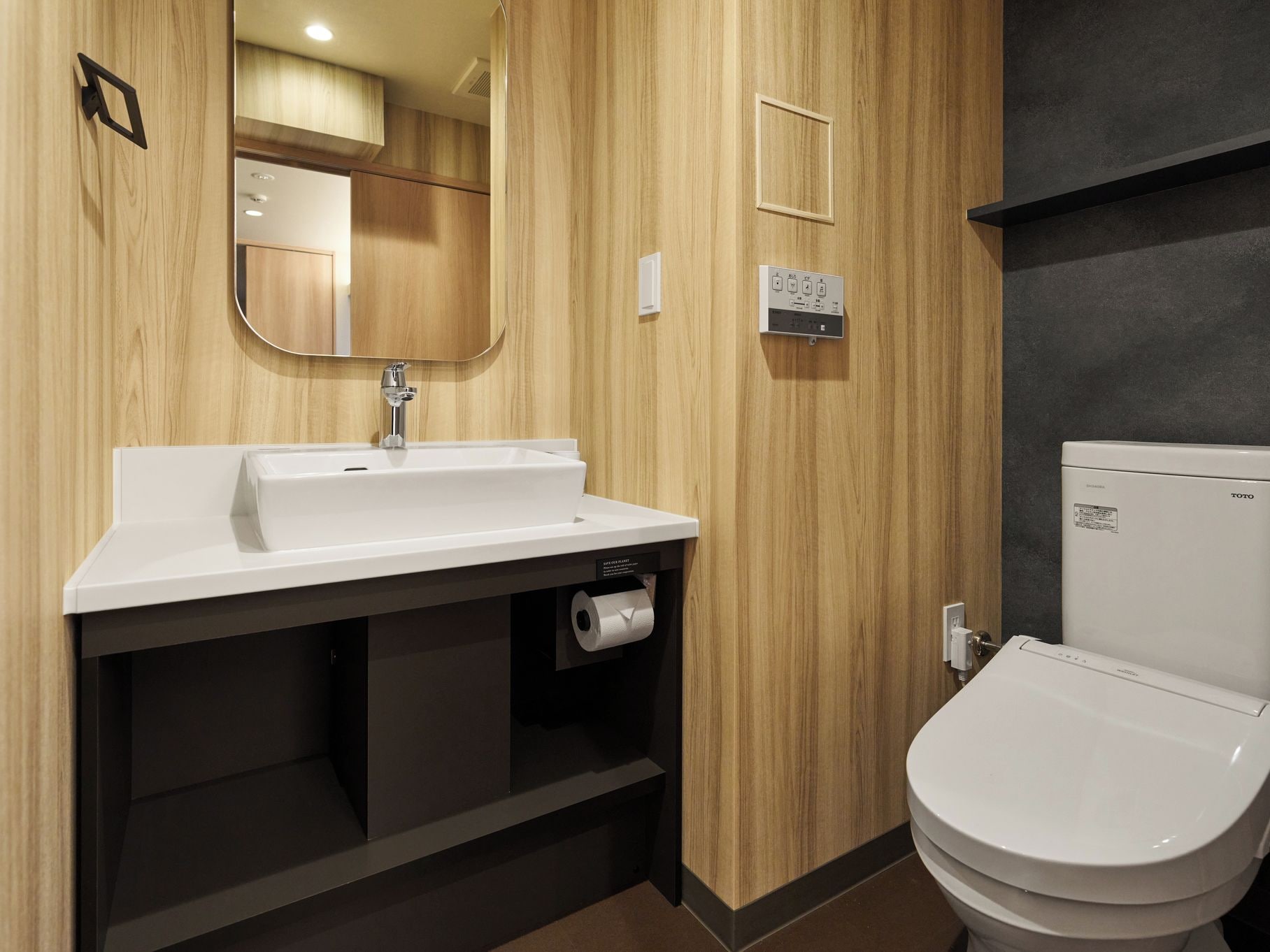 A modern bathroom with a wooden vanity, a sink, a toilet, and a mirror.
