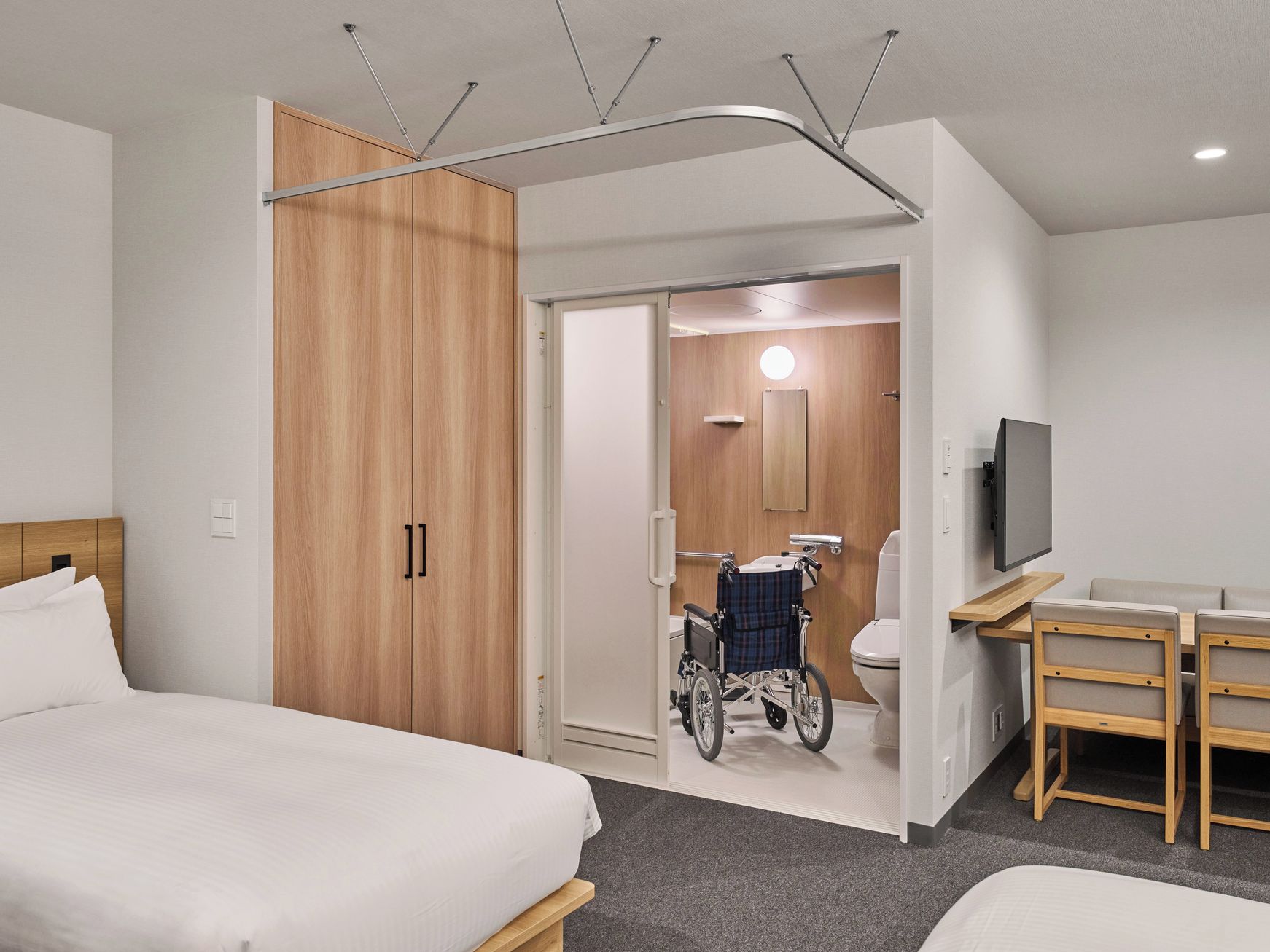 Ein Hotelzimmer mit Bett, Schreibtisch, Fernseher und einem Rollstuhl im Badezimmer.