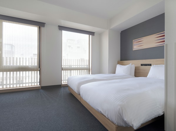 A hotel room with a large bed, two windows with blinds, a headboard with a control panel, and a painting on the wall.