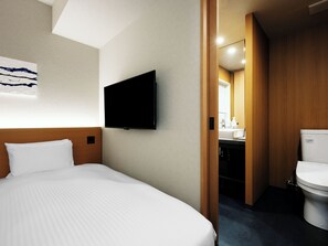 Een hotelkamer met een groot bed, een flatscreen televisie aan de muur en een badkamer door een geopende deur.