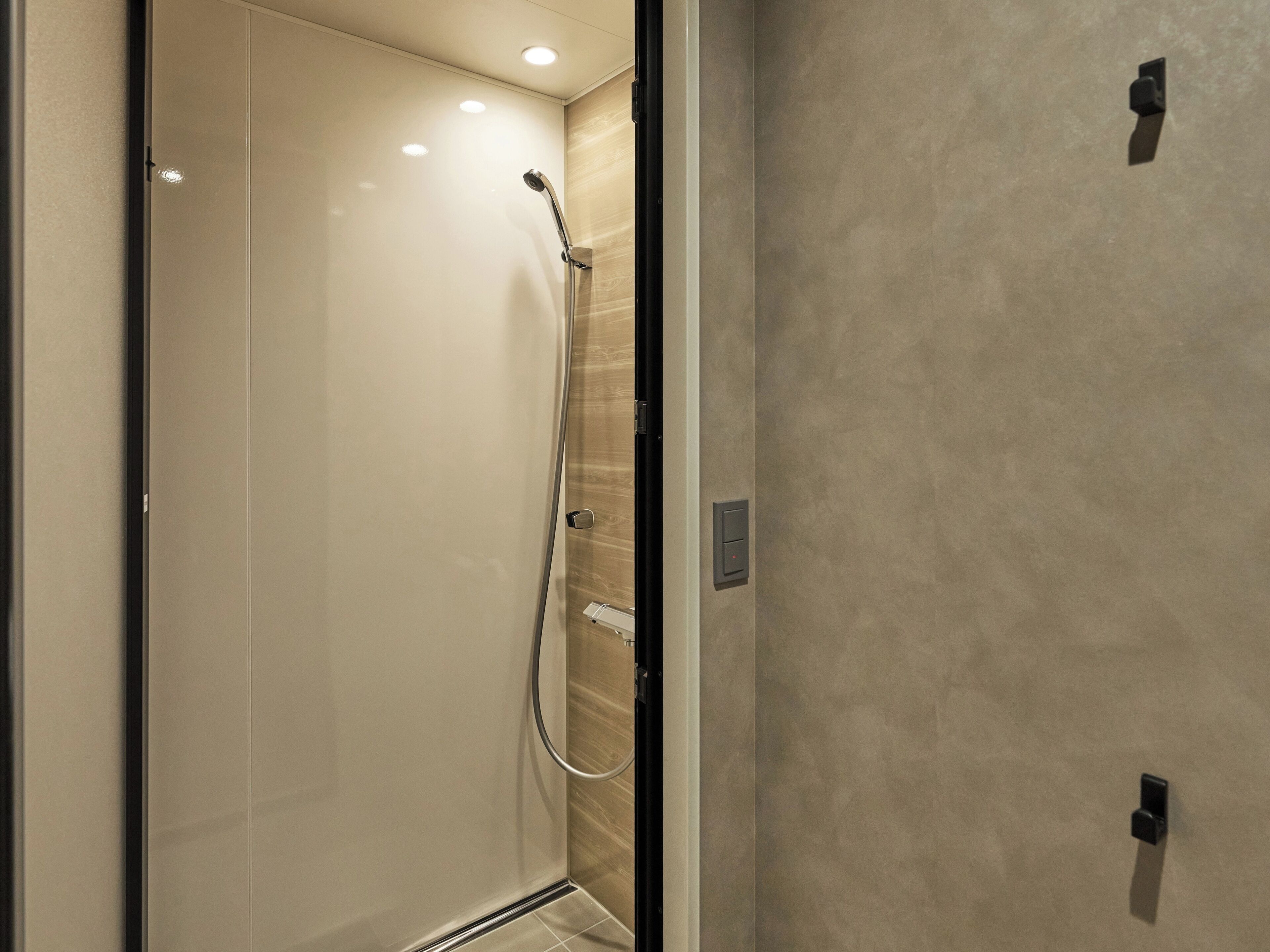 A modern bathroom with a glass-enclosed shower, a wall-mounted control panel, and a textured wall surface.