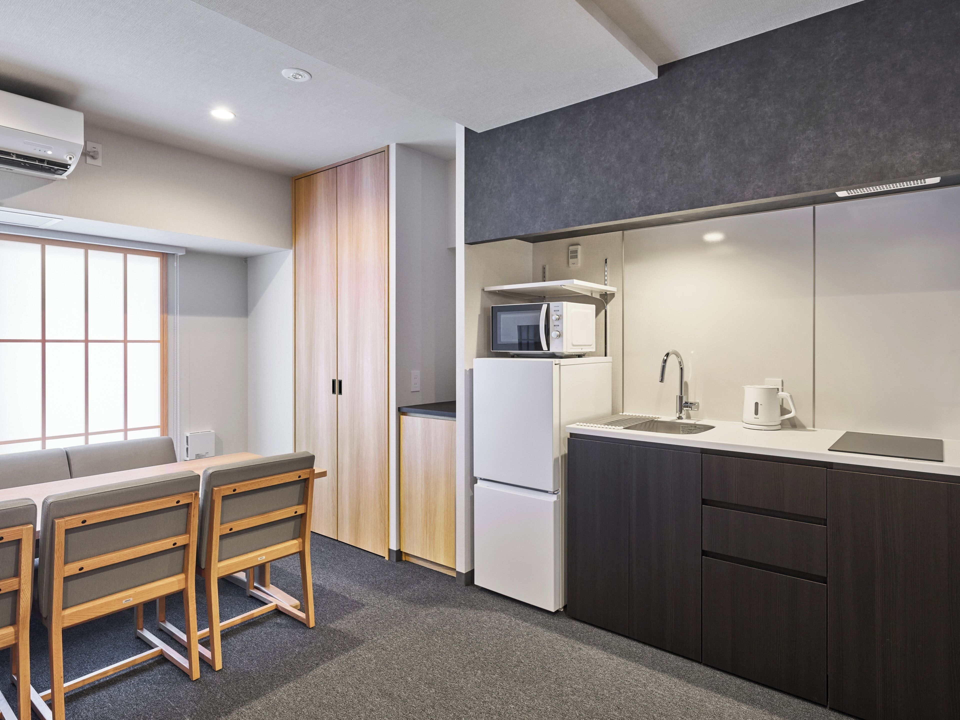 A modern kitchen with a microwave, refrigerator, and sink. There is a dining area with a table and chairs.