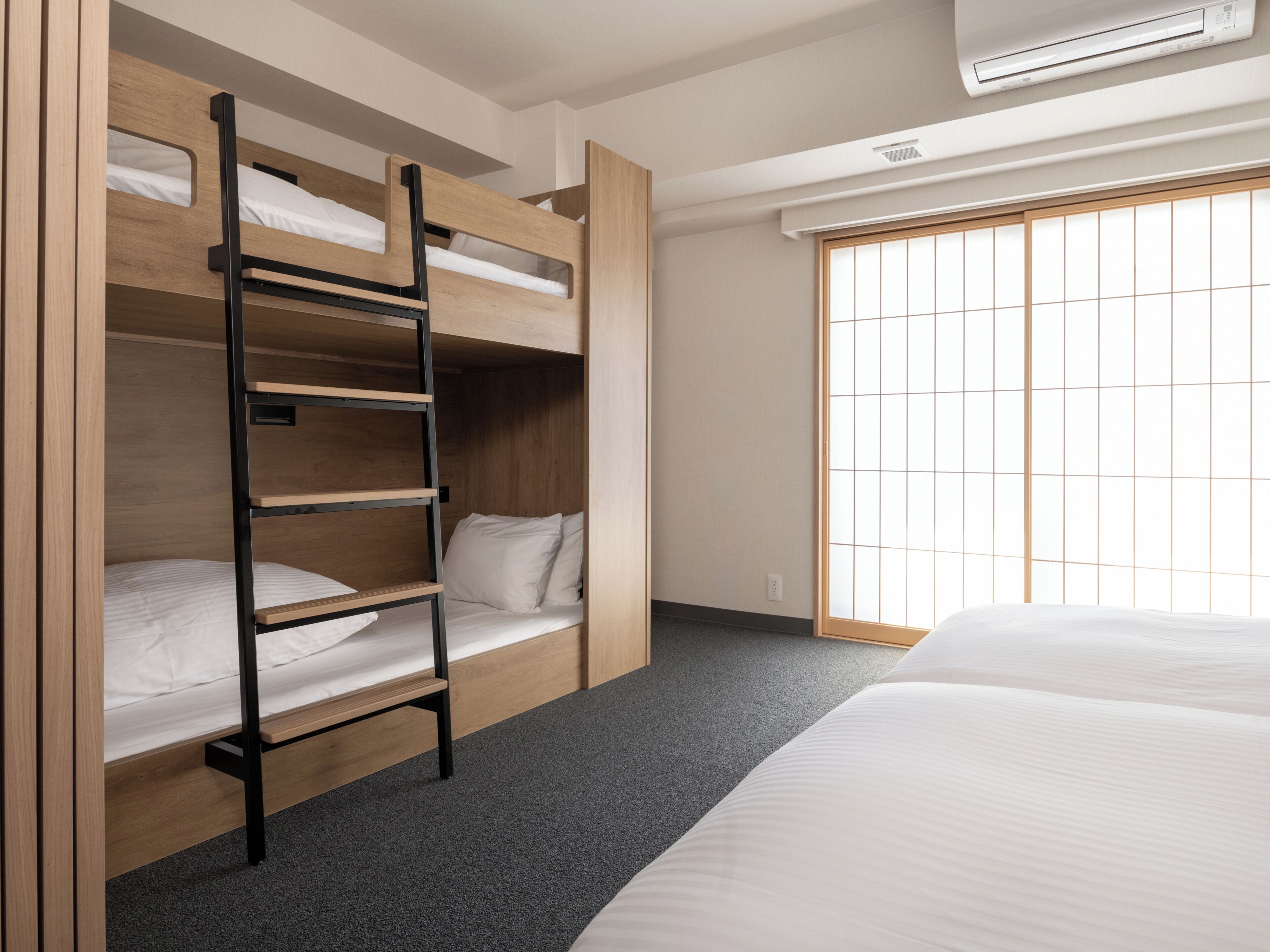 A bunk bed with a ladder, a window with a grid pattern, and an air conditioning unit.