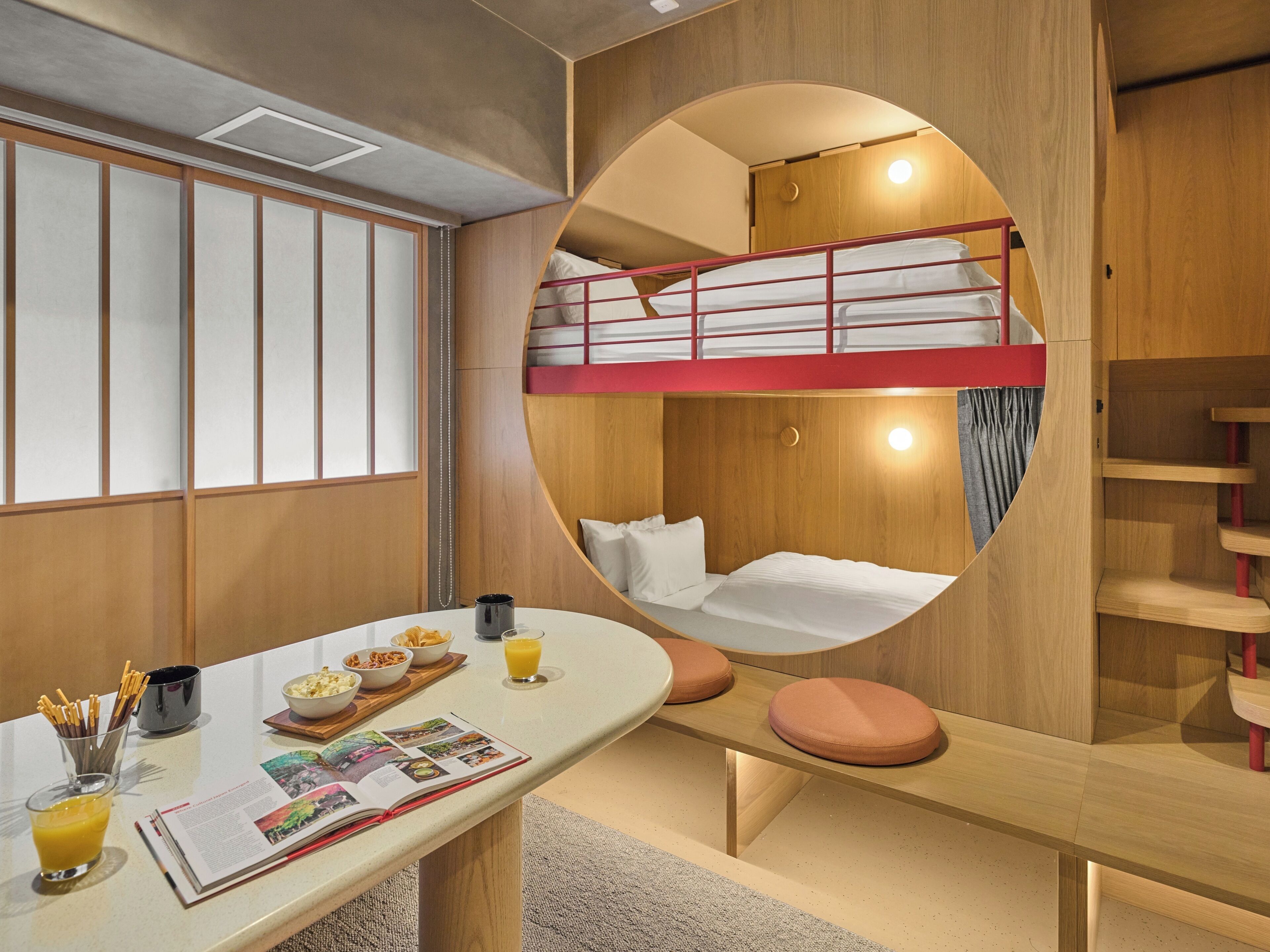 Habitación con literas, una ventana circular, una mesa de comedor con alimentos para el desayuno y una revista.