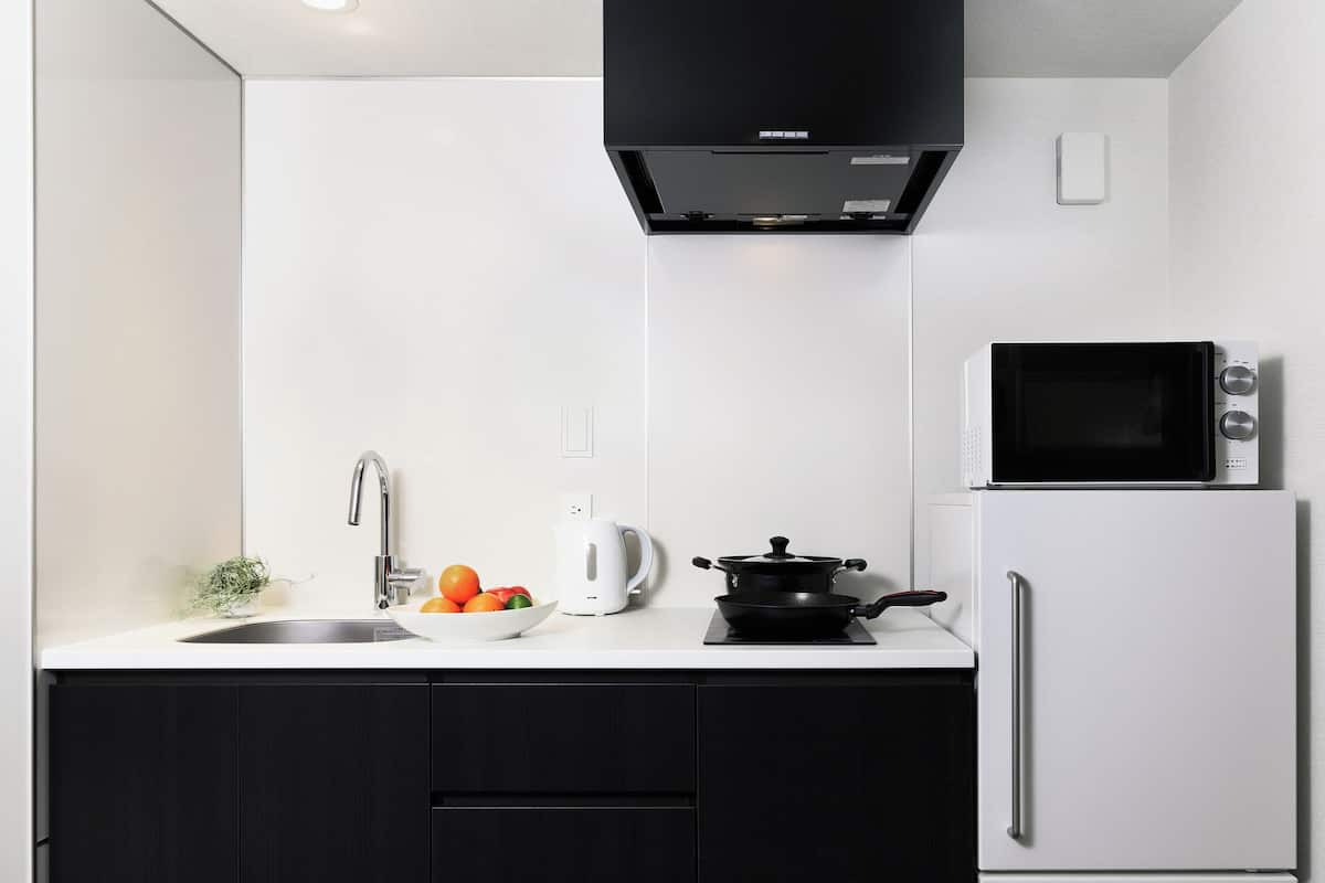 A modern kitchen with a white countertop, a black stove, a white kettle, and a microwave.