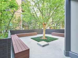 An outdoor courtyard with a central tree, surrounded by brick planters and seating areas. - MIMARU Osaka Shinsaibashi Central (Opens on September 1, 2026) (Osaka)