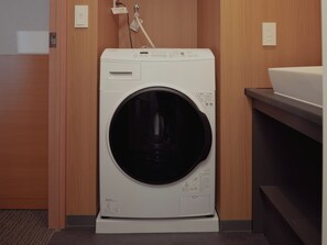 A compact, wall-mounted washing machine in a modern bathroom with wooden paneling and a countertop.