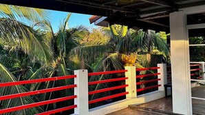 A covered outdoor area with a tiled floor, red railings, and palm trees in the background. - KNB West Villa Inn by SMS Hospitality (Bolinao)