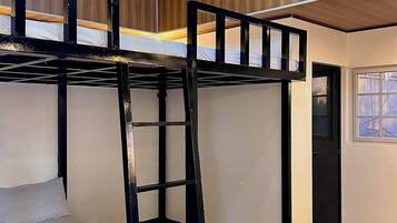 A bunk bed room with a ladder, wooden flooring, and a ceiling light fixture.