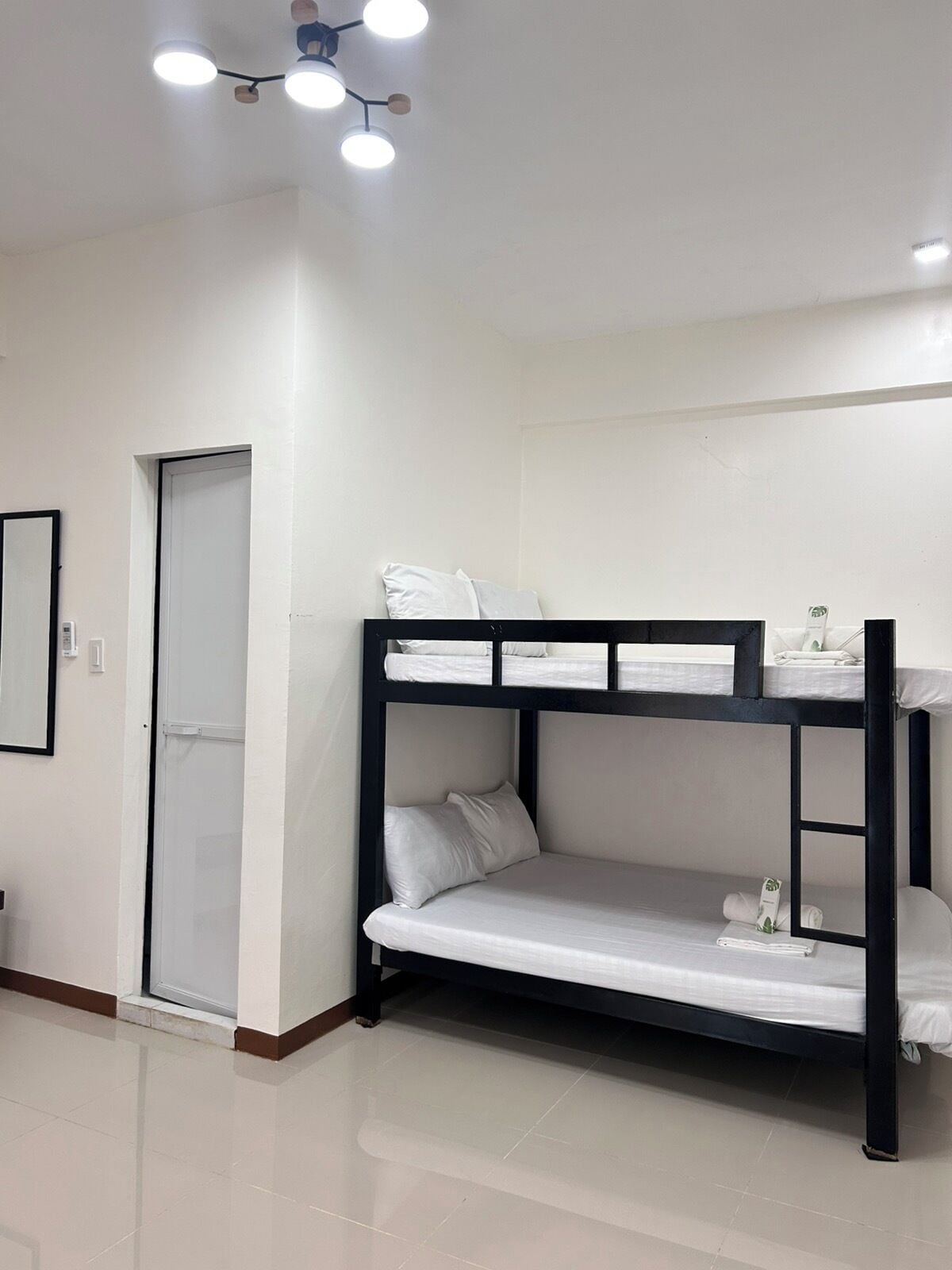 Una cama litera con ropa blanca, una lámpara en el techo y una puerta.