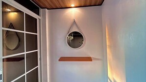 A room with a wooden ceiling, a white wall with a mirror and shelf, a sliding glass door, and a wooden floor. - KNB West Villa Inn by SMS Hospitality (Bolinao)