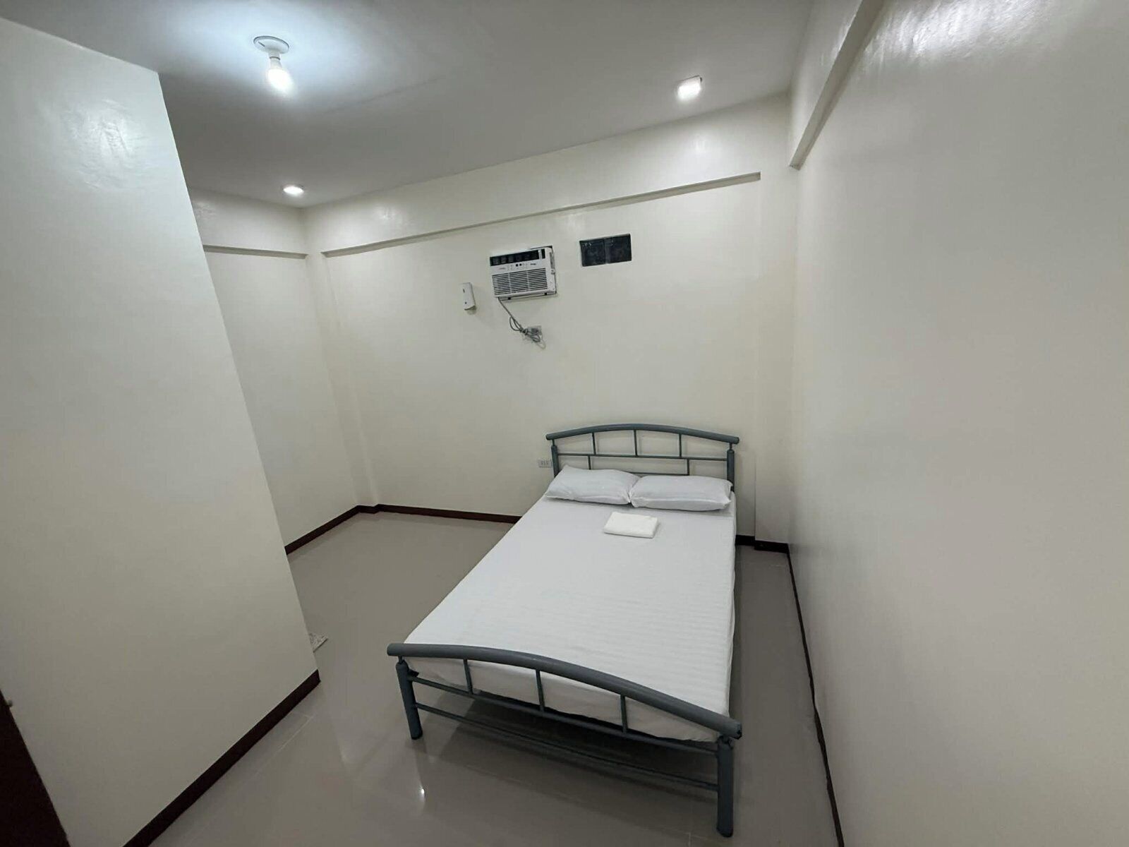 Una habitación pequeña y limpia con una cama individual, aire acondicionado de pared y una lámpara en el techo.