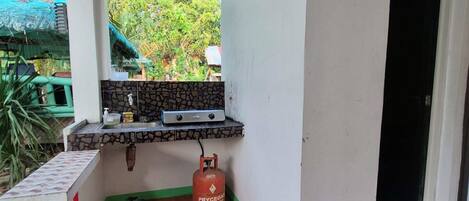 A small kitchen area with a gas stove, a gas cylinder, and a window overlooking greenery.