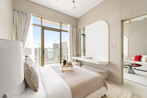 Une chambre d’hôtel moderne dotée d’un grand lit, d’un coin salon, d’une coiffeuse et offrant une vue sur la ville.