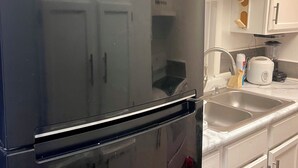 A kitchen with a black Whirlpool refrigerator, white cabinets, a double sink, and a countertop with various items. - Spacious2 - bedroom condo in tranquil (Reynoldsburg)